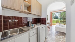 Une cuisine compacte équipée d’un évier, de placards et d’un petit réfrigérateur. On y trouve également un coin repas avec une table et des chaises, ainsi qu’un lit donnant sur l’extérieur.