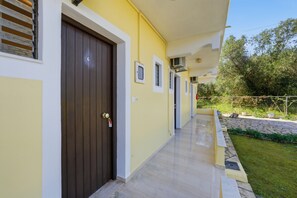 A corridor with a closed door, a small window, and an air conditioning unit on the wall.