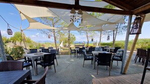 Une terrasse extérieure avec des tables et des chaises, ombragée par de grands auvents, et offrant une vue sur la campagne.