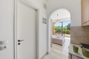 Une chambre d’hôtel comprenant un lit, un coin repas avec une table et des chaises, un coin cuisine avec une cuisinière et un plan de travail, et un balcon extérieur offrant une vue sur la verdure.