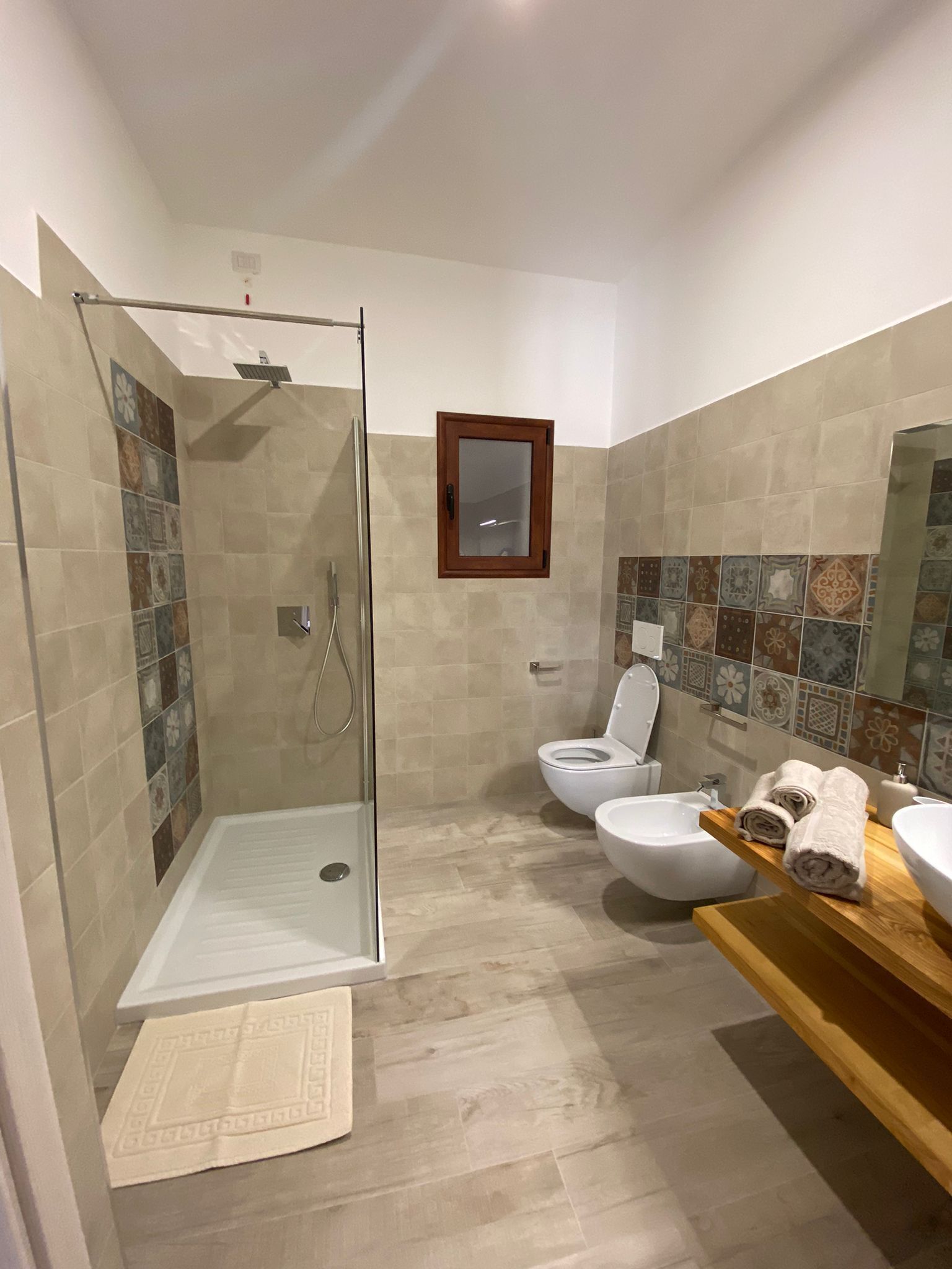 Une salle de bain moderne avec une douche en verre, deux toilettes, un lavabo et un meuble-lavabo en bois agrémenté de serviettes.