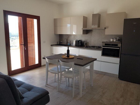 Une cuisine moderne avec des meubles blancs, une table à manger avec des chaises, un réfrigérateur noir et une cuisinière.