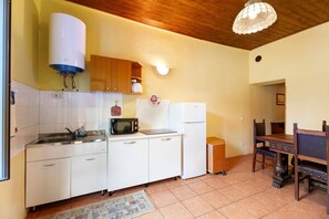 Eine kompakte Küche mit weißen Schränken, einer Mikrowelle, einem Kühlschrank und einem Durchlauferhitzer.