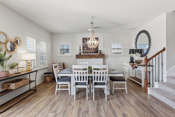 A dining area with a white table, four chairs, a chandelier, and a fireplace.