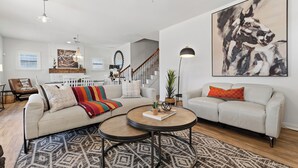Un salón amplio con un cuadro grande, dos sofás, una mesa de centro y una escalera que conduce al piso superior.