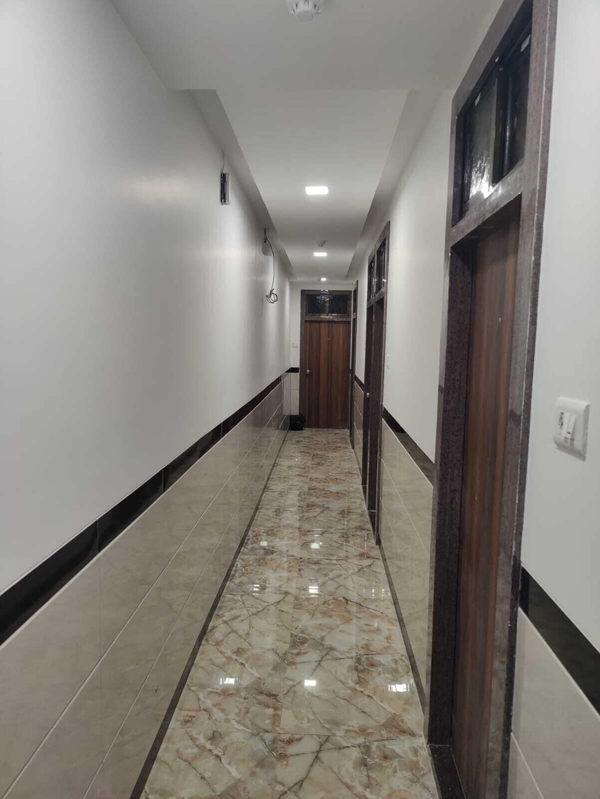 Un pasillo con piso de mármol, paredes blancas y una puerta de madera al final.