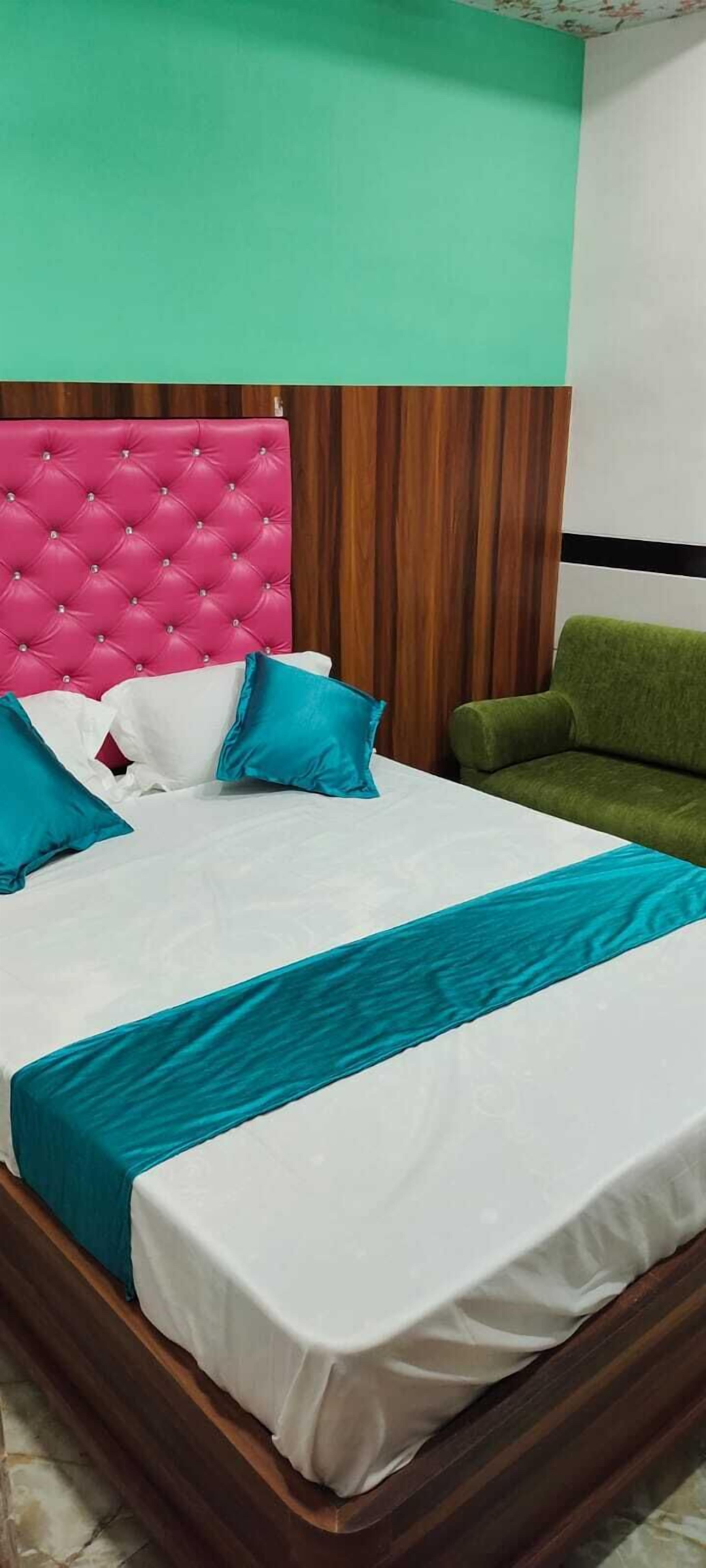 A bed with a pink tufted headboard, white and teal bedding, and a green armchair.