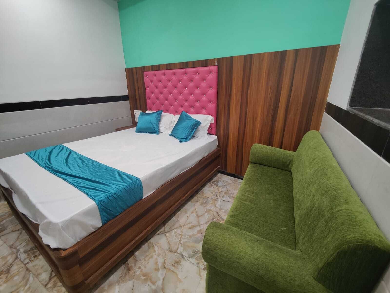 A single bed with a wooden frame and a pink tufted headboard, accompanied by two blue pillows. A green upholstered chair is positioned to the right.