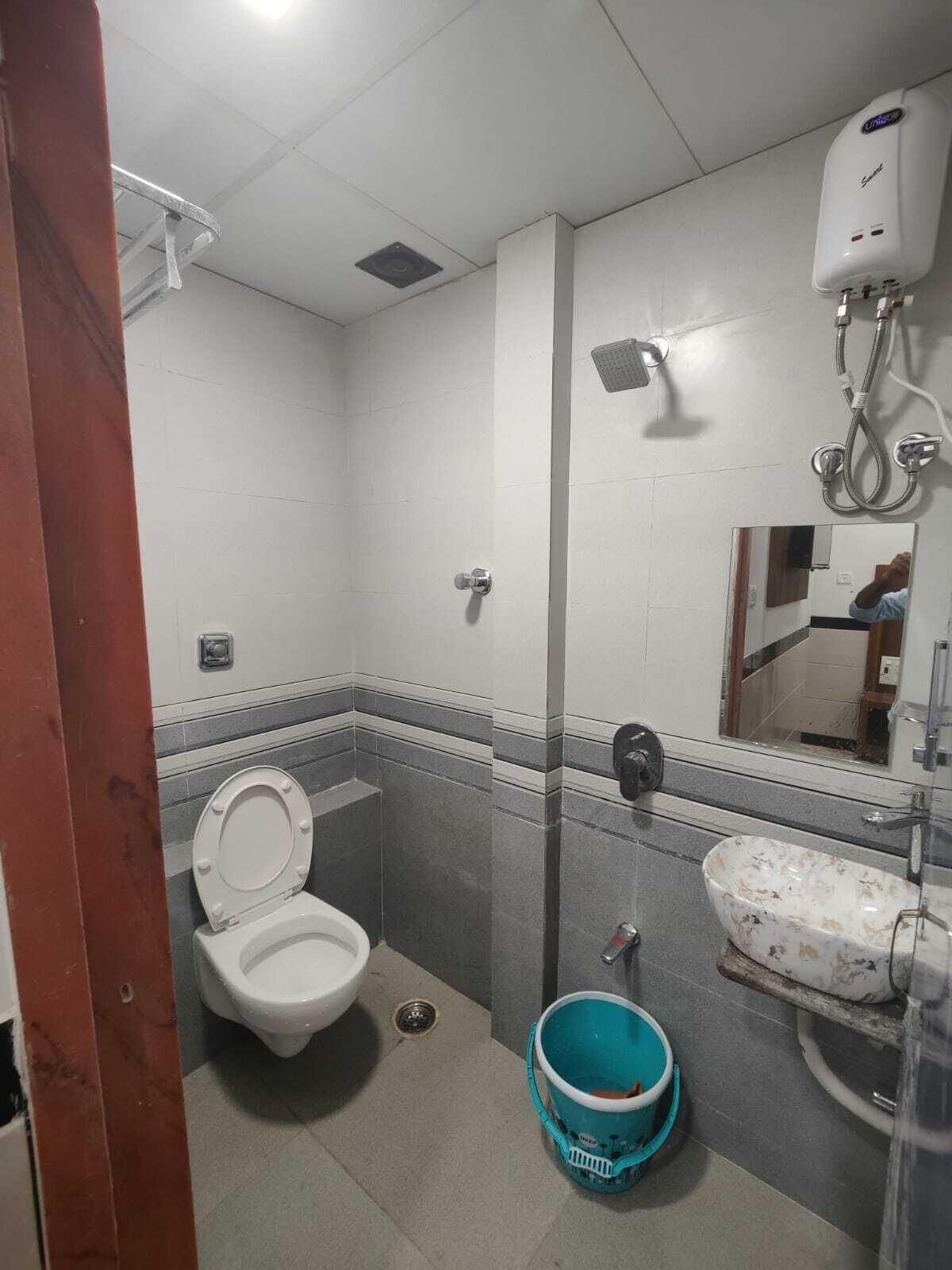 A bathroom with a toilet, a sink, a shower, and a bucket.