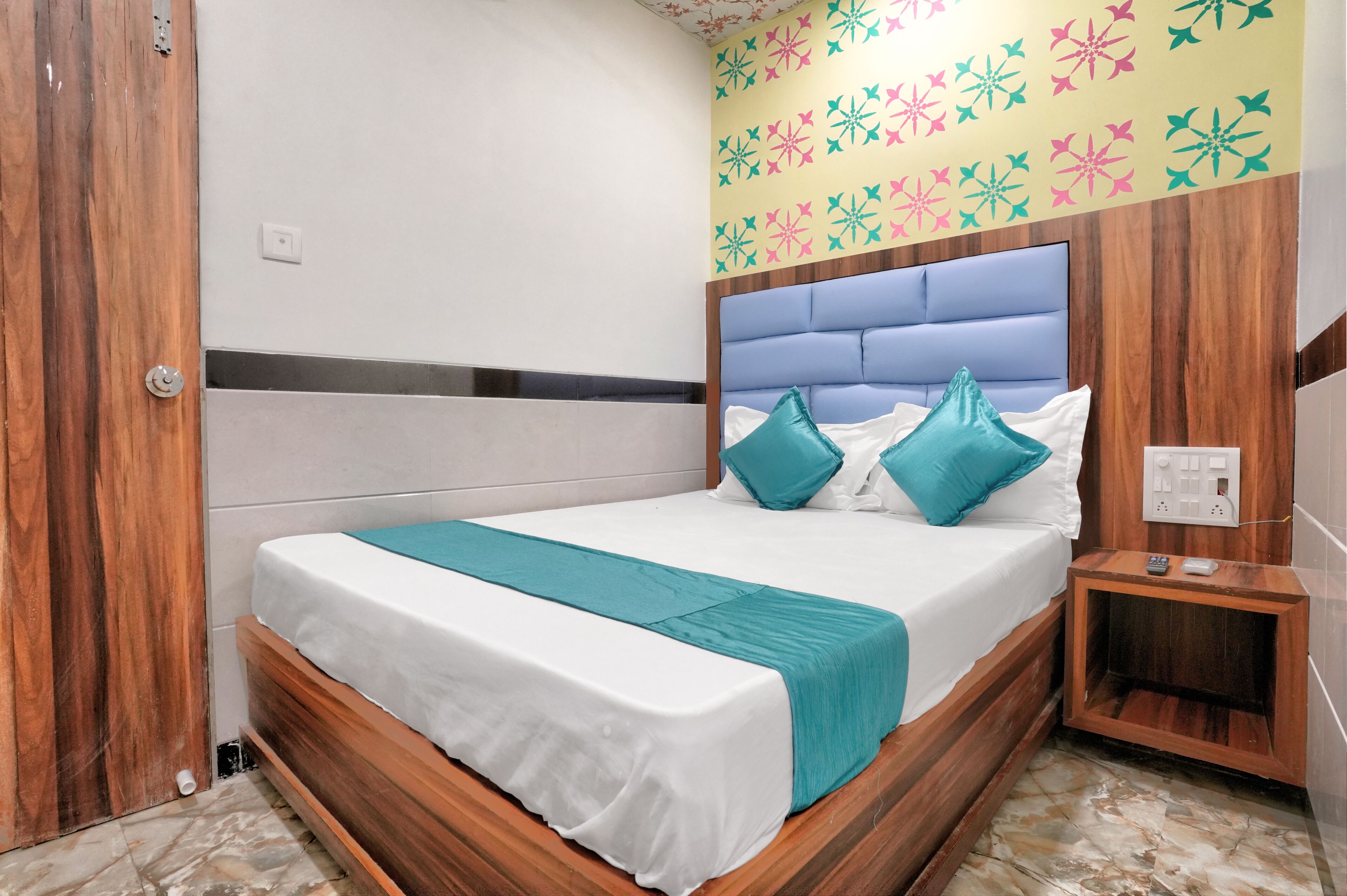 A neatly made bed with a wooden headboard, a teal throw blanket, and two teal pillows.