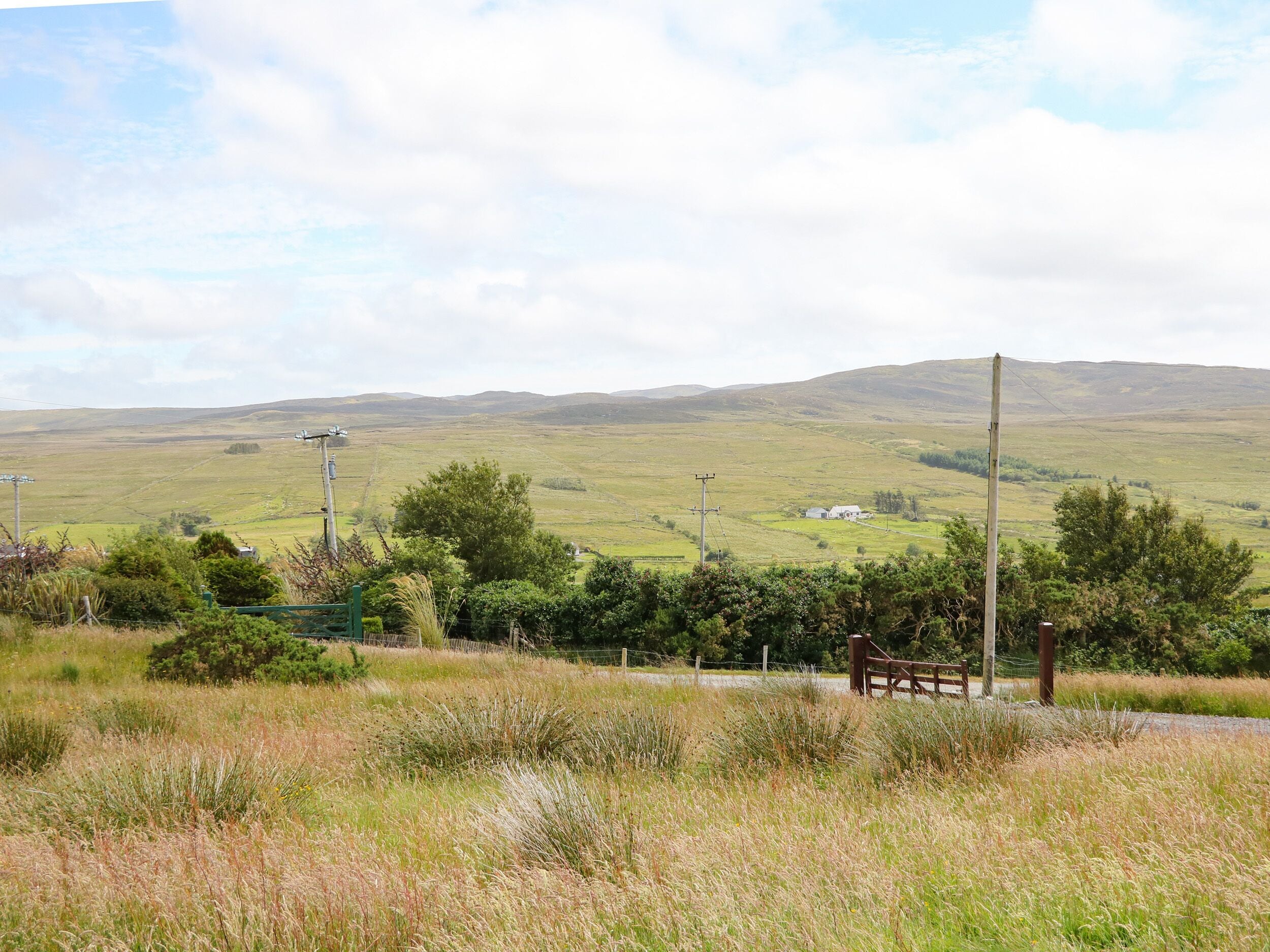 A rural landscape with rolling hills, a small house, and a fence in the foreground.