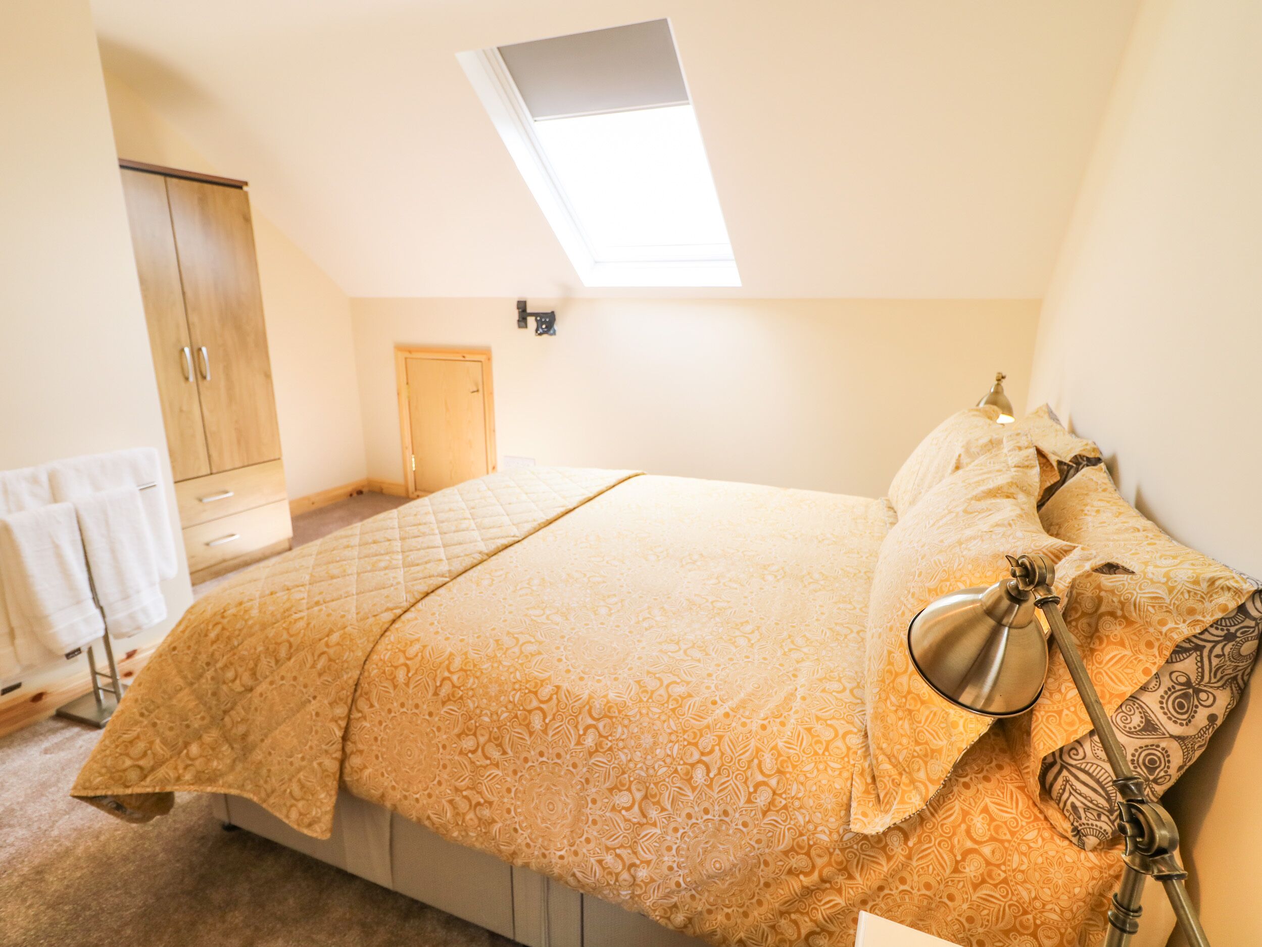 A bedroom with a bed, a skylight, a wardrobe, and a nightstand.