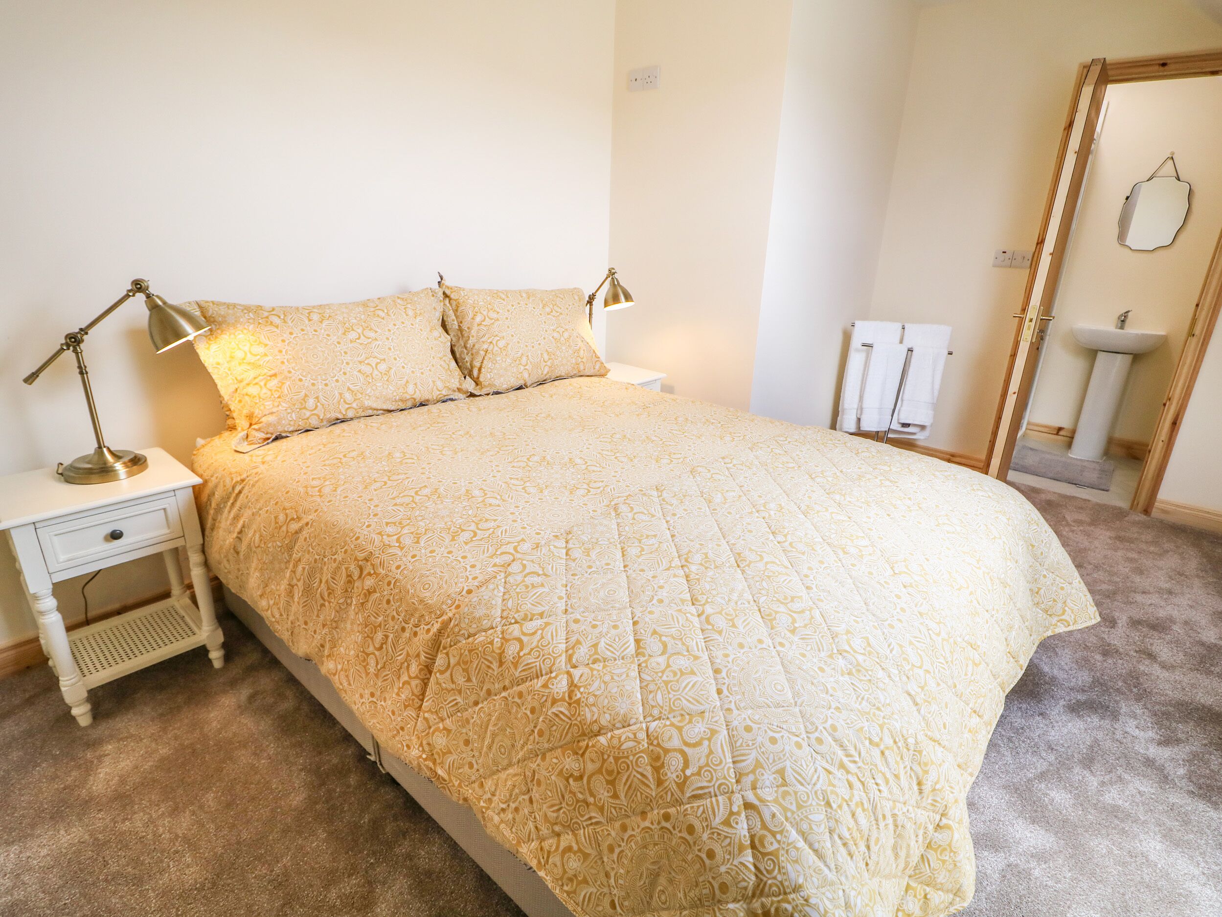 A neatly made bed with a patterned bedspread, a bedside lamp, and a nightstand with a drawer.