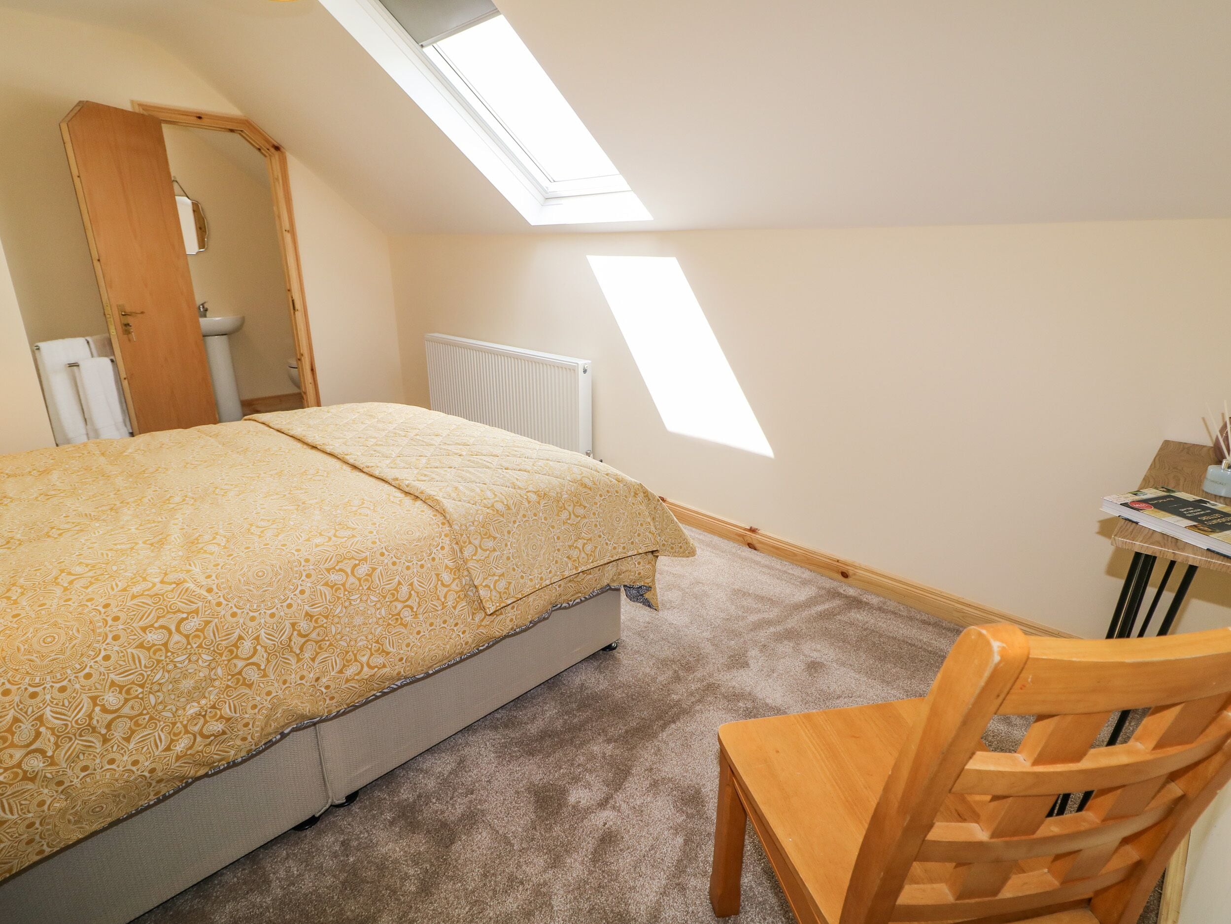 A bedroom with a bed, a chair, a desk, and a skylight.