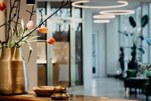 A reception area with a vase of flowers, a wooden bowl, and a bell on a counter. - Hotel Crystal (Saarbrücken)