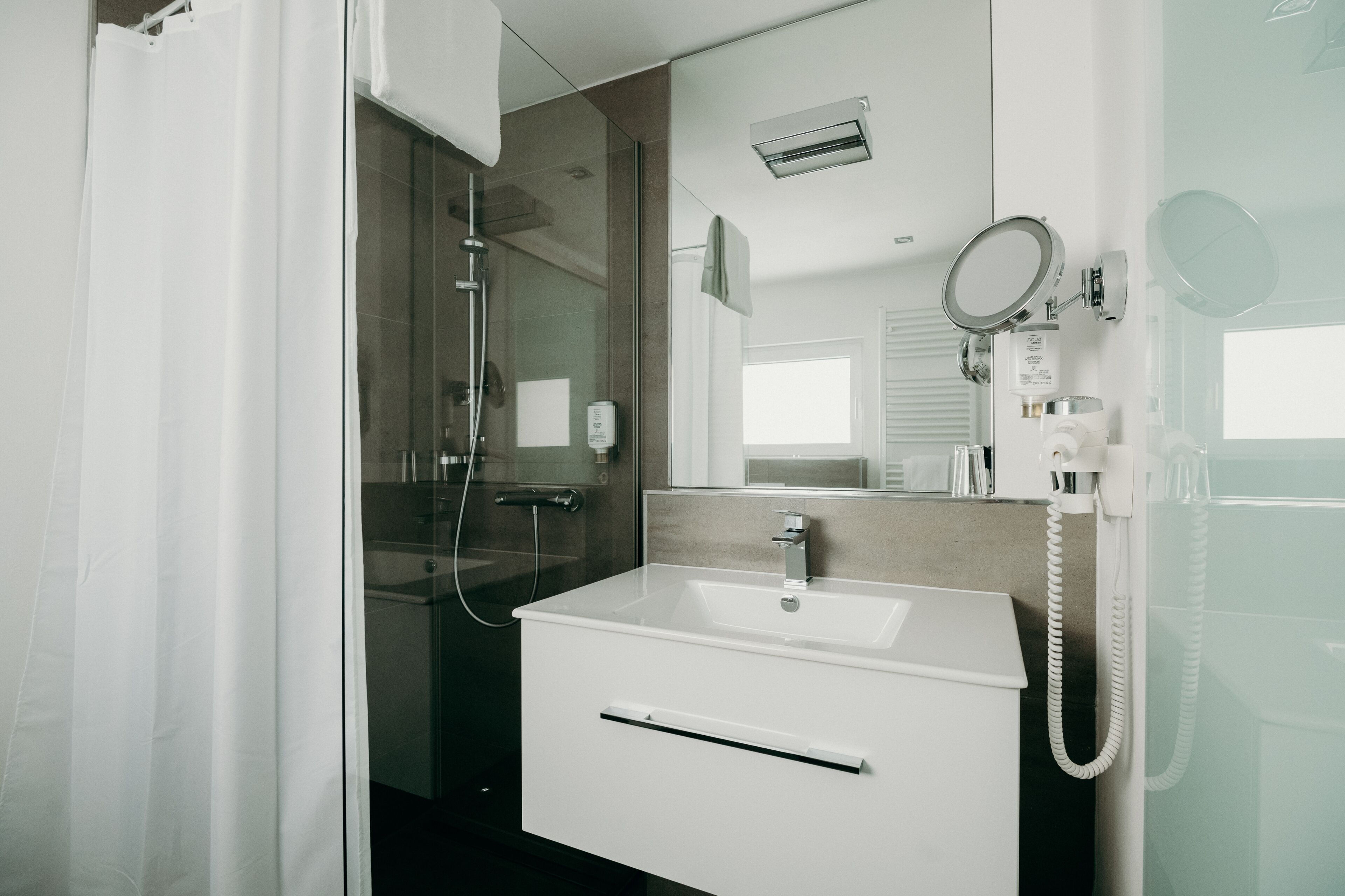 A modern bathroom with a glass shower enclosure, a white sink, and a mirror with a mounted telephone.