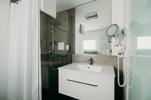 Un baño moderno con cabina de ducha de vidrio, un lavamanos blanco y un espejo con teléfono integrado.