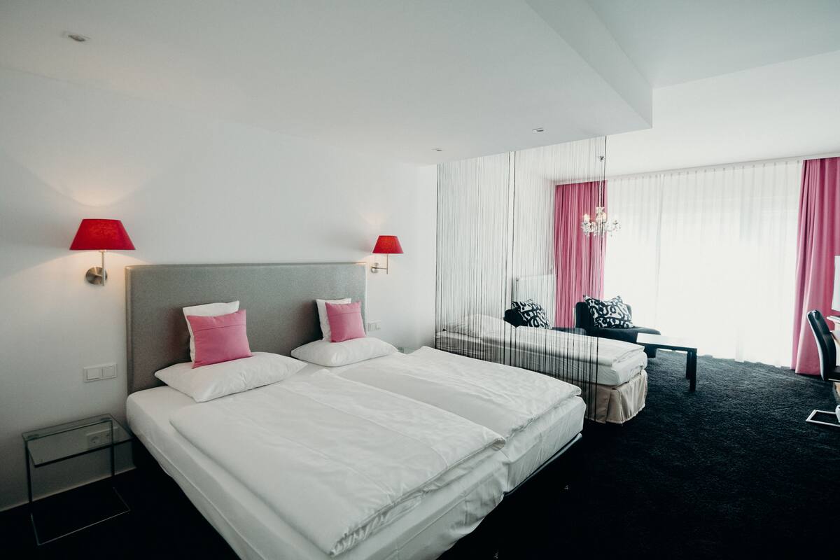 A hotel room with two beds, a desk, a chair, and a large window with curtains.
