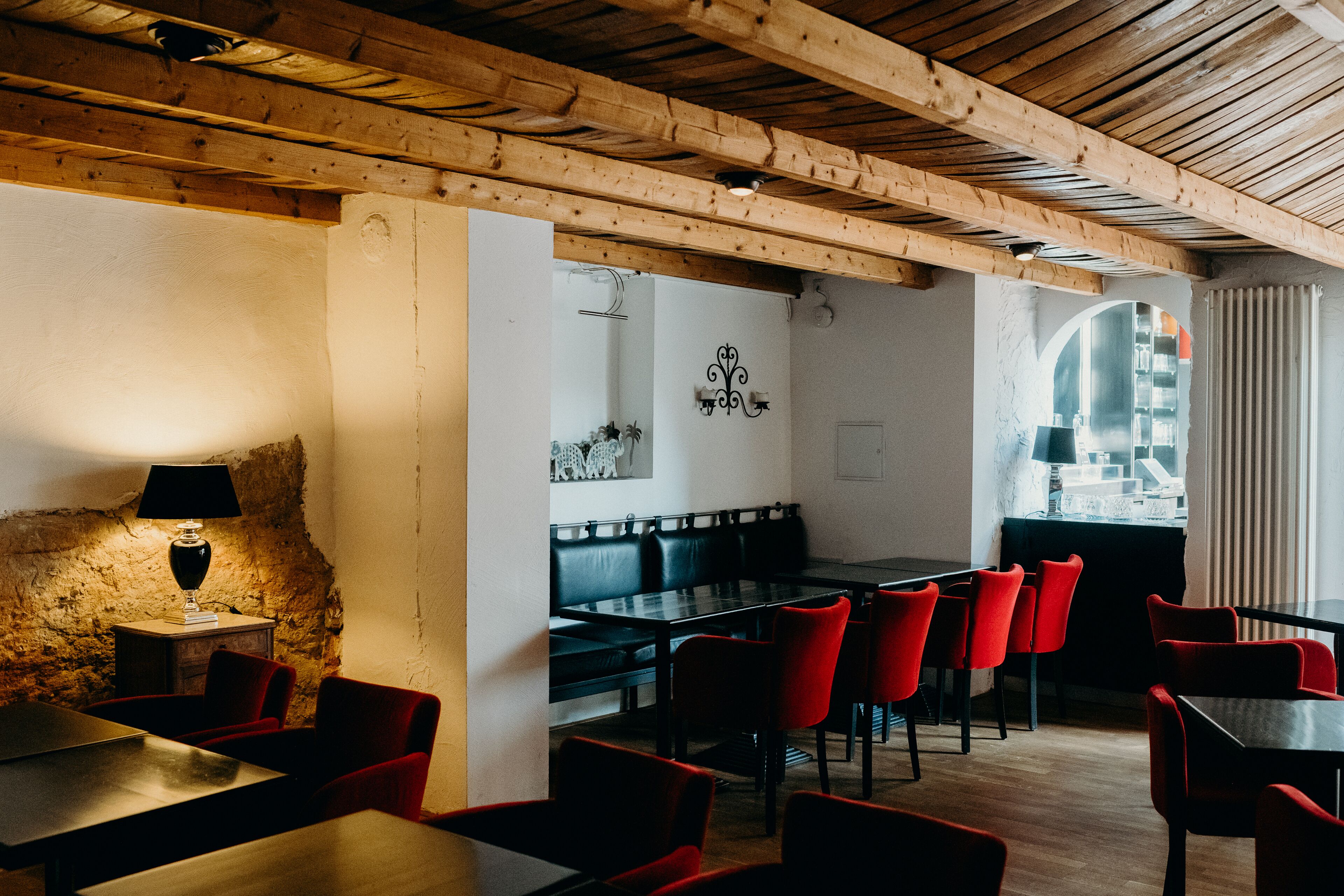 A restaurant with wooden beams, red and black chairs, and a stone wall.