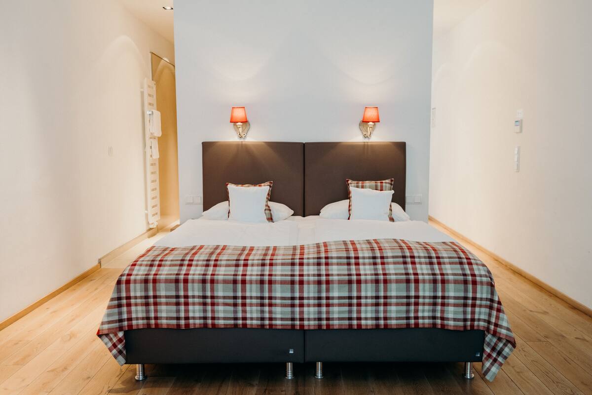 A modern bedroom with a large bed, two bedside lamps, and a wooden floor.