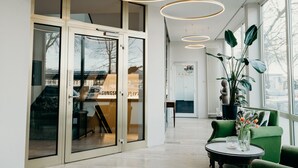 A modern interior with glass doors, a green sofa, and a round table with a vase. - Hotel Crystal (Saarbrücken)