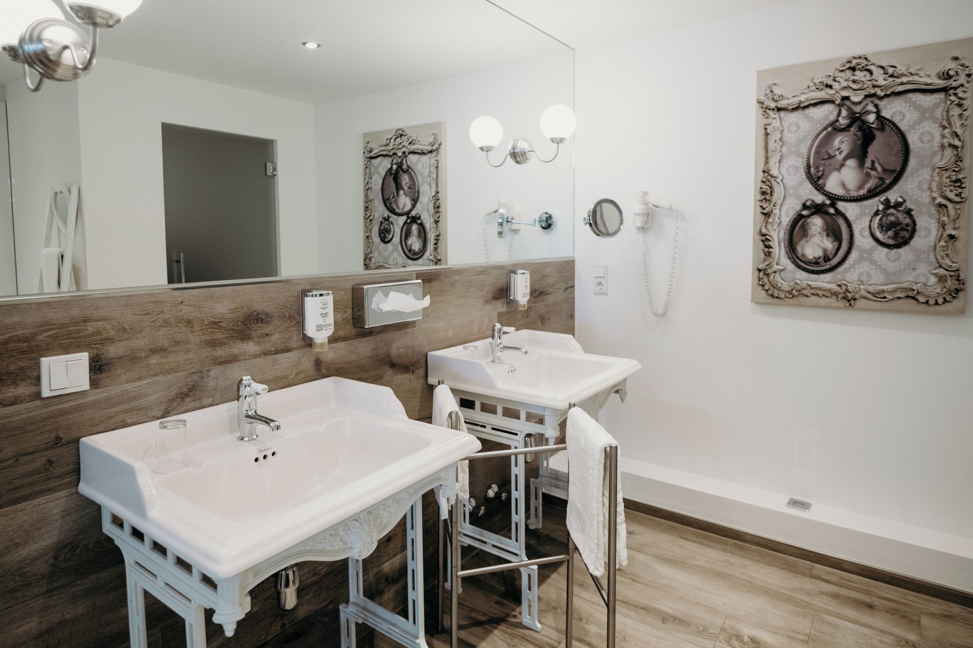 A bathroom with two sinks, a mirror, wall-mounted lights, and a decorative frame.