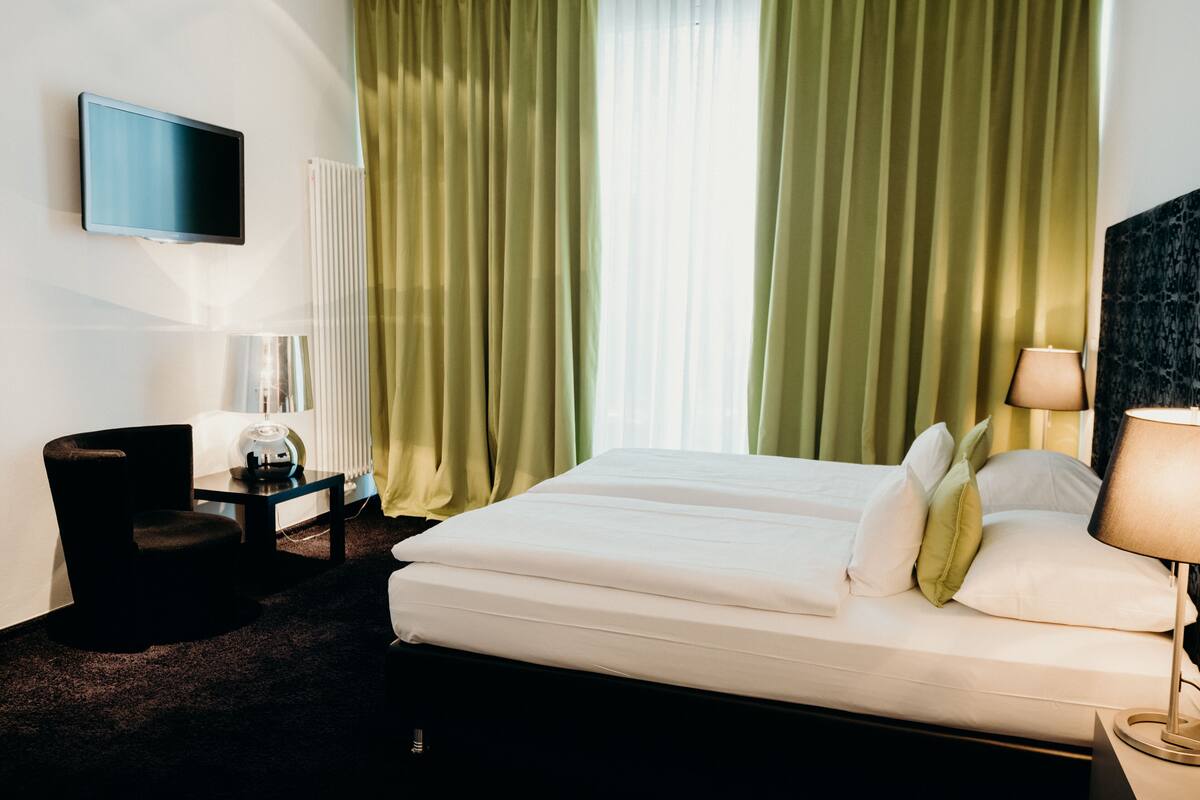 A hotel room with a bed, a desk, a chair, a TV, and curtains.