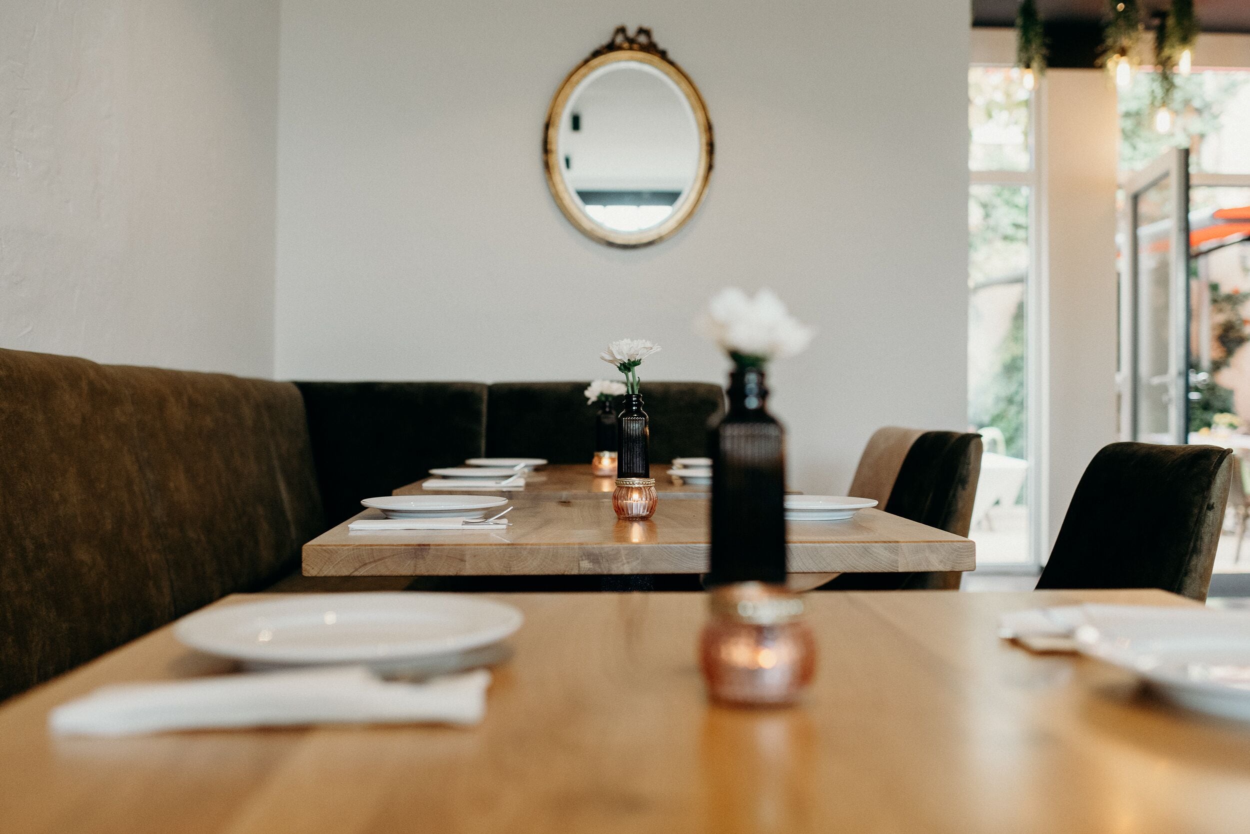 Un coin repas avec une table en bois dressée pour deux personnes, un miroir au mur et une vue sur l’extérieur.