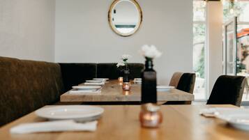 A dining area with a wooden table set for two, a mirror on the wall, and a view of the outdoors.