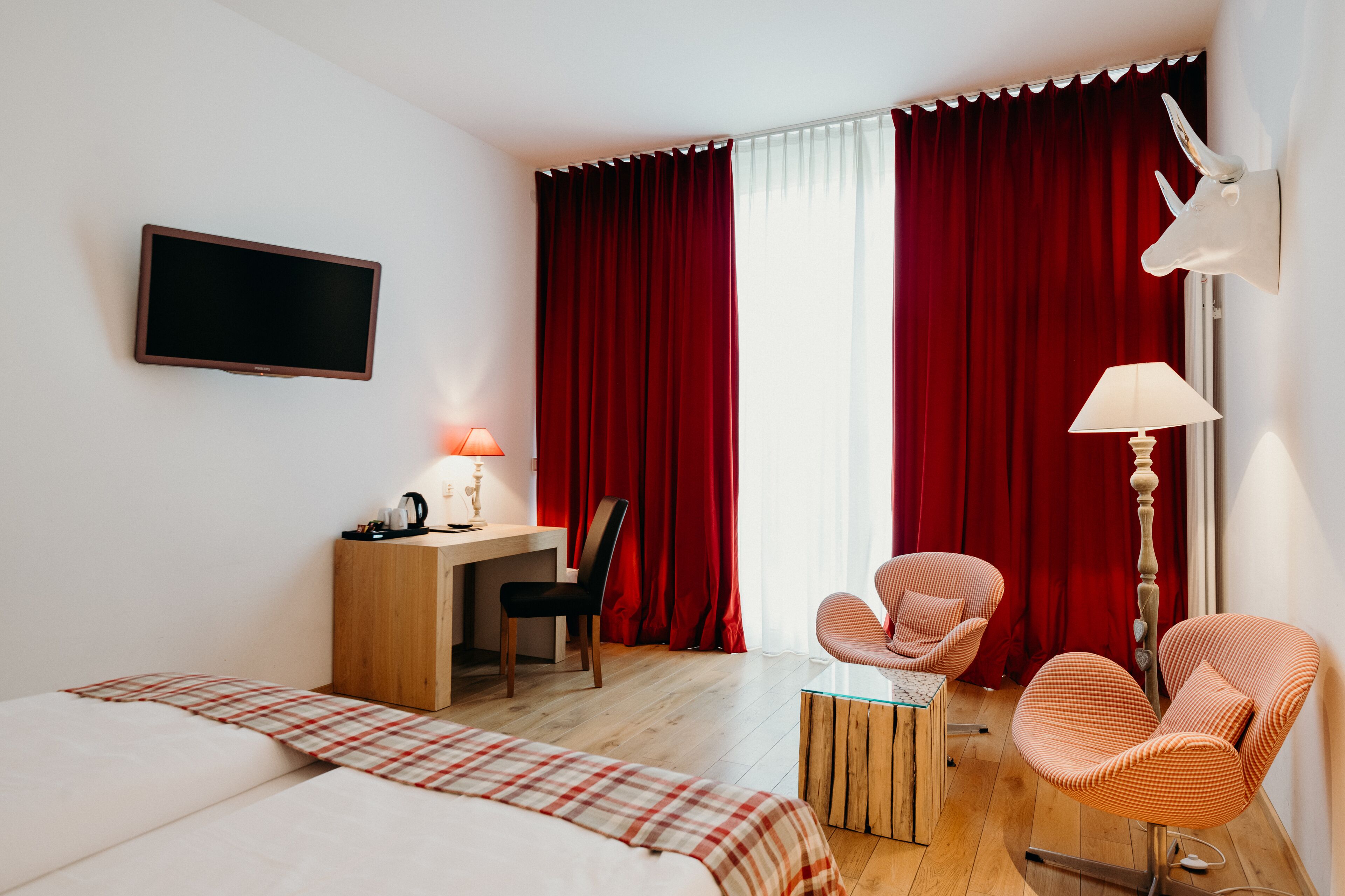 Camera d'albergo con due letti, una scrivania con lampada, una sedia e una decorazione raffigurante una testa di animale appesa al muro.
