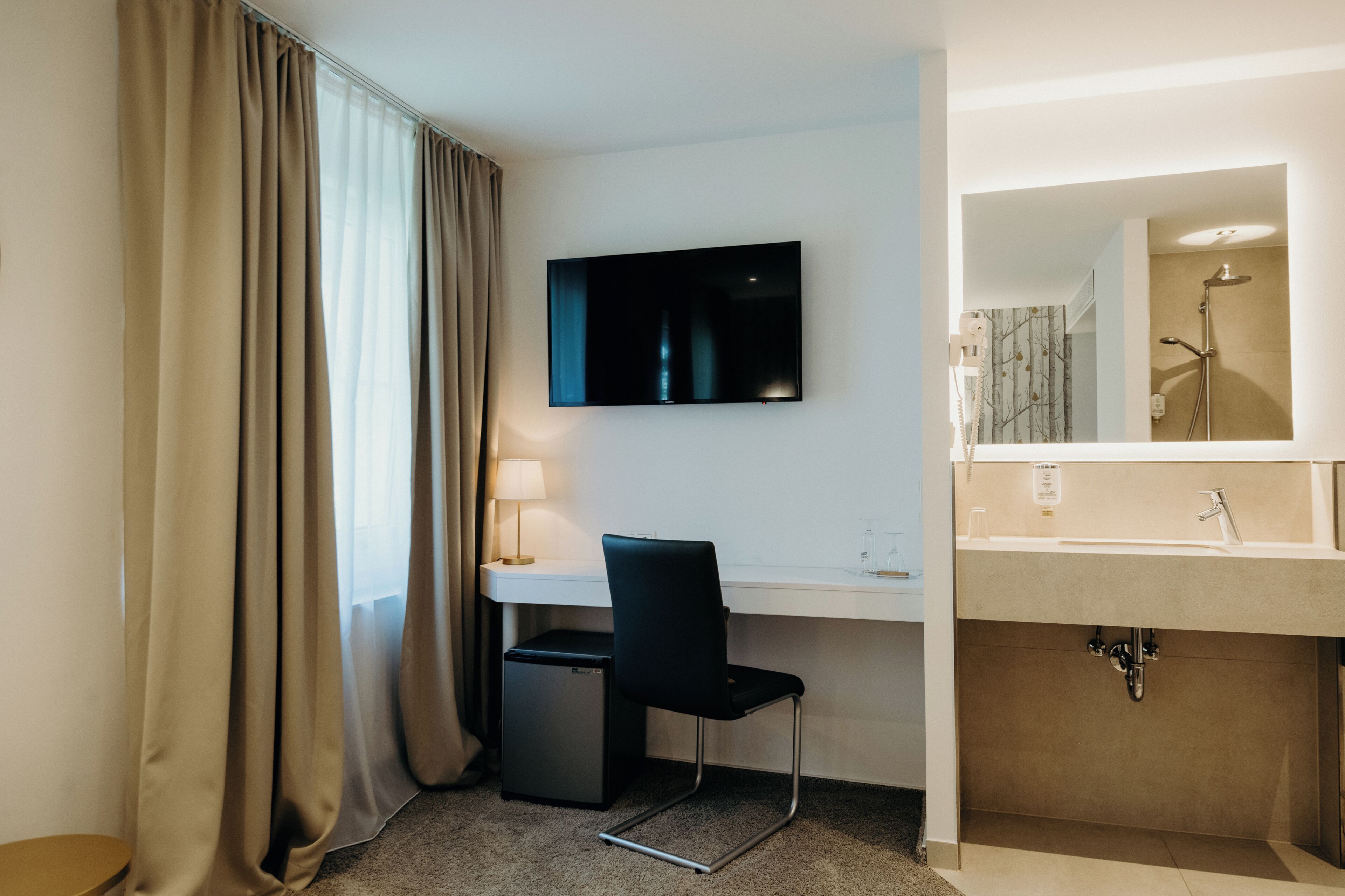 Habitación de hotel con escritorio, silla, televisión y baño con lavabo y espejo.