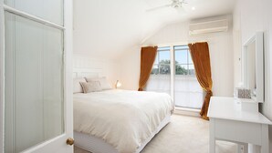 A bedroom with a bed, a bedside table, a mirror, and a window with curtains.
