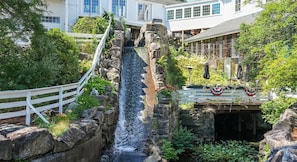 A waterfall feature with a white fence, surrounded by greenery and a building with large windows.