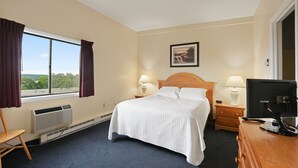 Ein Hotelzimmer mit einem Bett, zwei Nachttischlampen, einem Fernseher, einem Fenster mit Vorhängen und einem Bild an der Wand.