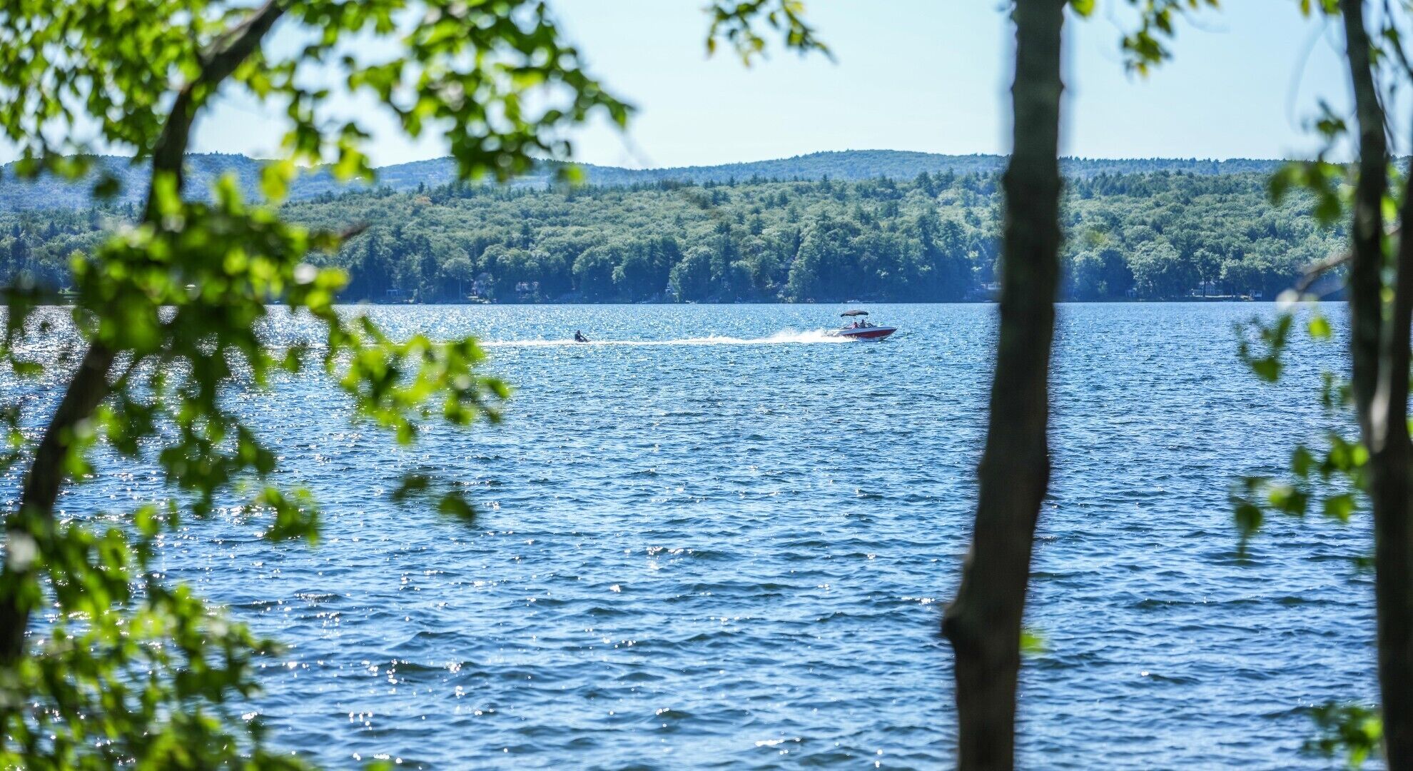 A lake with a boat in the distance and a forested hill in the background.