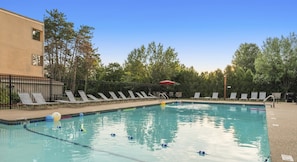 A swimming pool with lounge chairs and a fence, surrounded by trees.