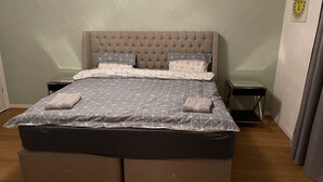 Ein Schlafzimmer mit einer gesteppten Kopfteil, einem Bett mit einem geometrisch gemusterten Bettbezug, zwei Nachttischen und einer kleinen Wanddekoration.