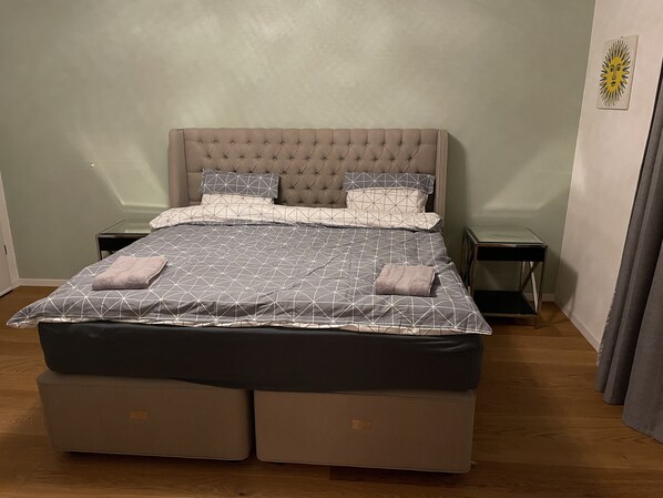 A bedroom with a tufted headboard, a bed with a geometric patterned bedspread, two bedside tables, and a small wall decoration.