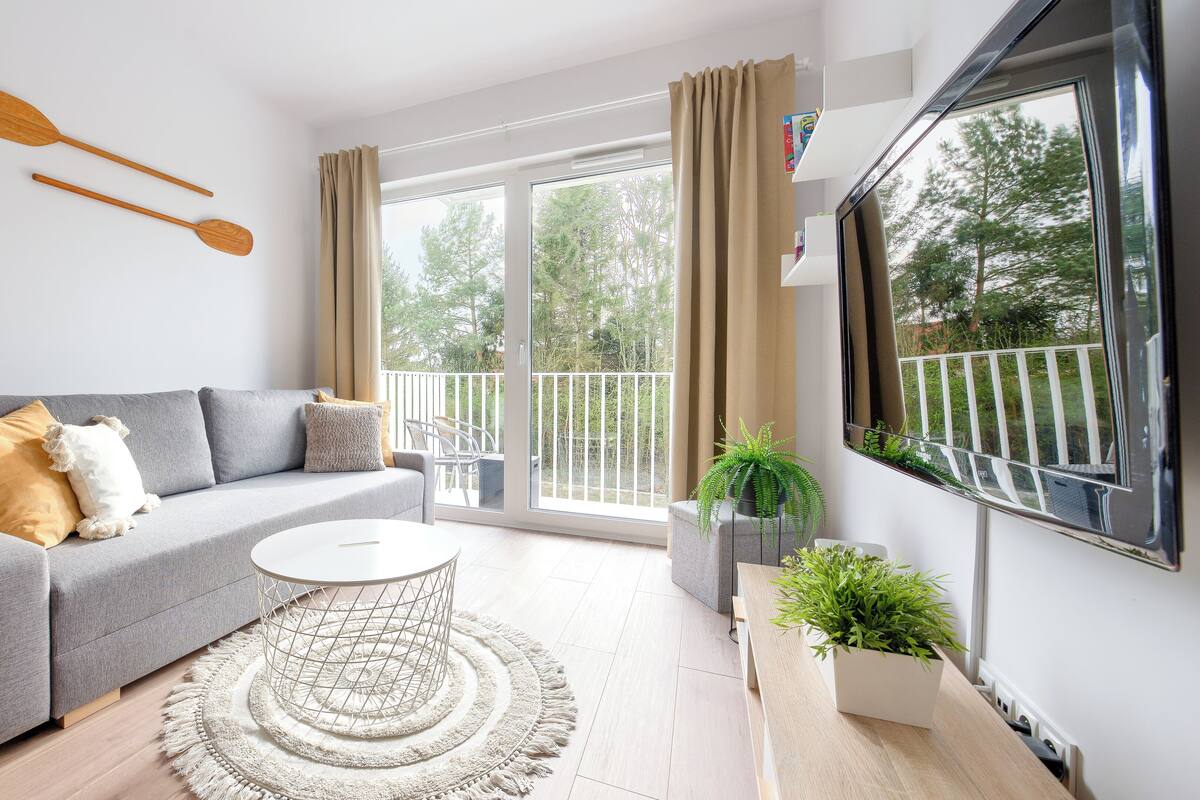 A modern living room with a grey sofa, a round coffee table, and a large window with curtains.