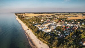 Vista aérea de uma cidade costeira com praia, edifícios residenciais e turbinas eólicas ao longe.