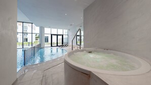 Uma piscina interna com hidromassagem, janelas amplas e vista para o exterior.