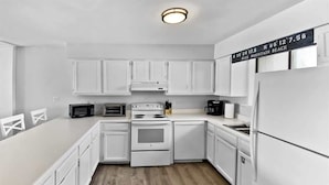 A kitchen with white cabinets, a stove, a microwave, and a refrigerator.