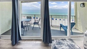 A balcony with a view of the sea, a table with chairs, and a rug.