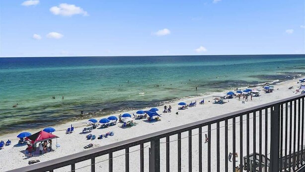 A beach with umbrellas and lounge chairs, a railing, and the ocean.