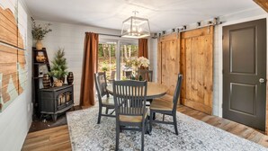 Un coin repas comprenant une table ronde, quatre chaises, un lustre, un buffet en bois et une porte coulissante de style rustique.