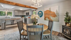 Une cuisine moderne avec des poutres en bois, un coin repas avec une table ronde et des chaises, et une grande fenêtre qui laisse entrer la lumière naturelle.