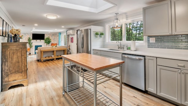 Une cuisine moderne dotée d’une verrière, d’appareils électroménagers en acier inoxydable et d’une table à manger en bois.