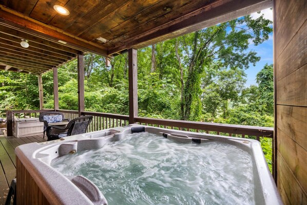 A hot tub under a wooden pergola with a view of a forest.