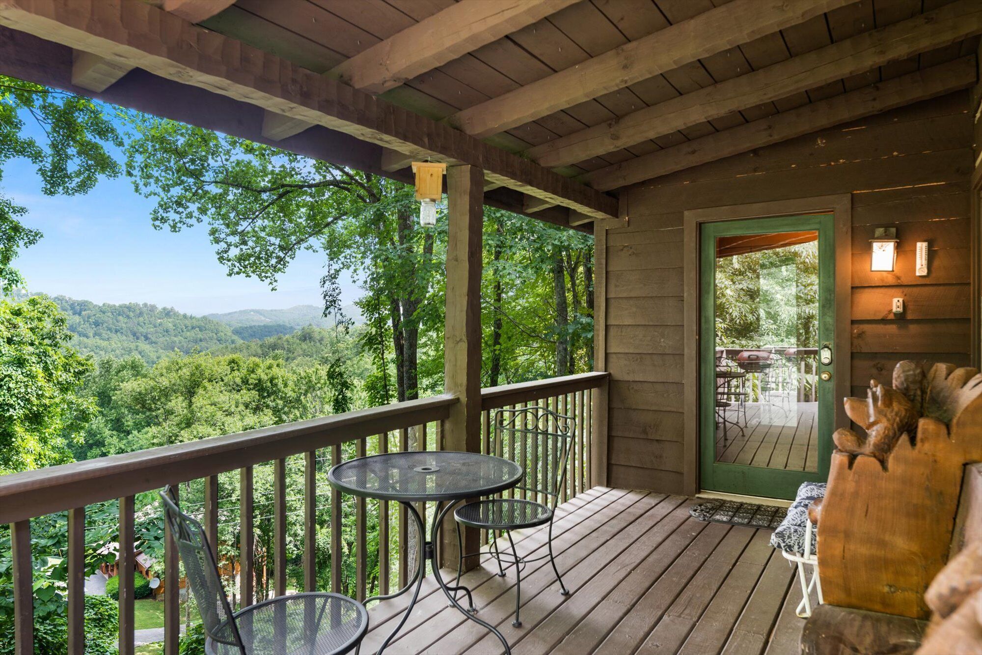 A wooden deck with two metal tables and chairs, overlooking a forested valley.