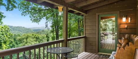 A wooden deck with two metal tables and chairs, overlooking a forested valley.